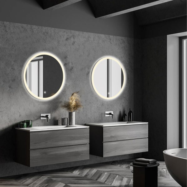 Modernes Badezimmer mit zwei runden beleuchteten Wandspiegeln und zwei hängenden Waschtischunterschränken vor einer Betonwand.