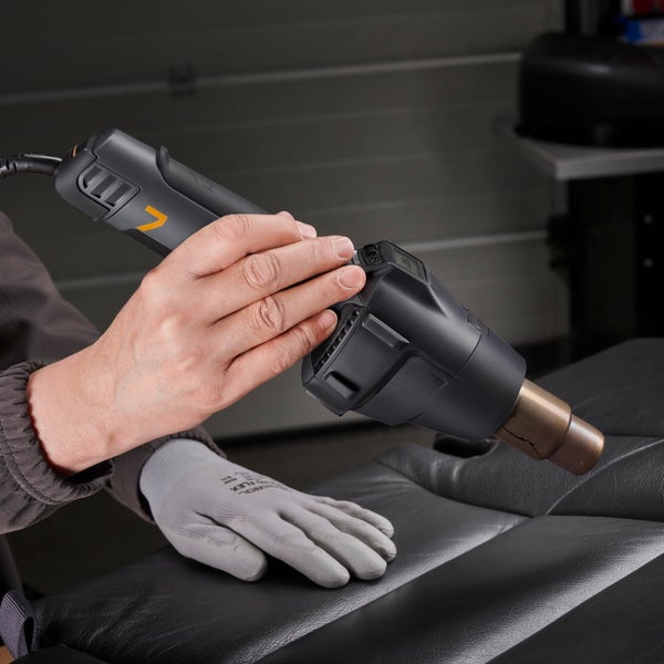 Heißluftgebläse in der Hand eines Arbeiters bei der Anwendung auf einer Lederoberfläche.