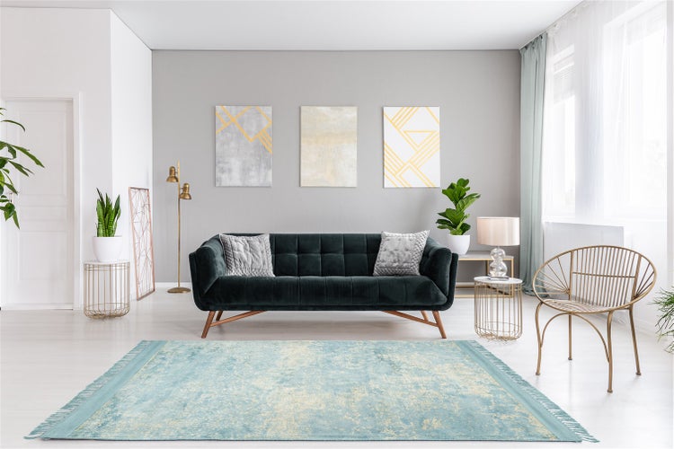 Helles, modernes Wohnzimmer mit dunkelgrünem Samtsofa, blauem Vintage-Teppich, goldenem Metallsessel und abstrakten Wandbildern.