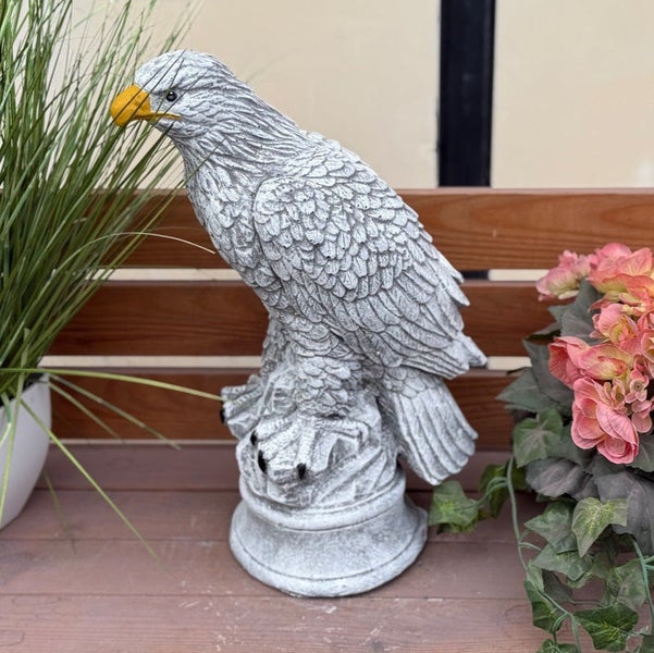 Gartenfigur Adler aus Steinguss in Grau auf rundem Sockel, sitzend mit gelbem Schnabel.