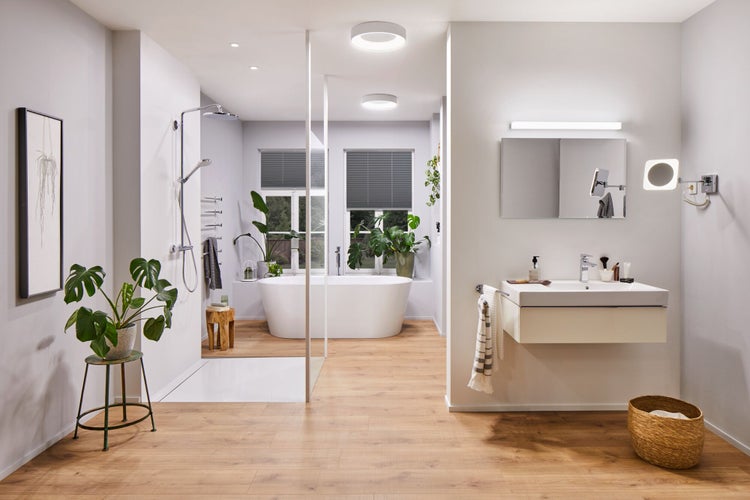 Modernes Badezimmer mit freistehender Badewanne, bodengleicher Dusche, Waschtisch mit Spiegel und Holzoptik Fliesenboden in einem hellen Raum.