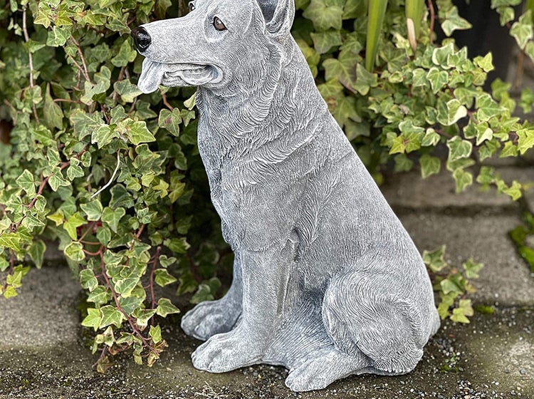 Steinfigur in Form eines sitzenden Schäferhundes als Gartendekoration vor Efeu