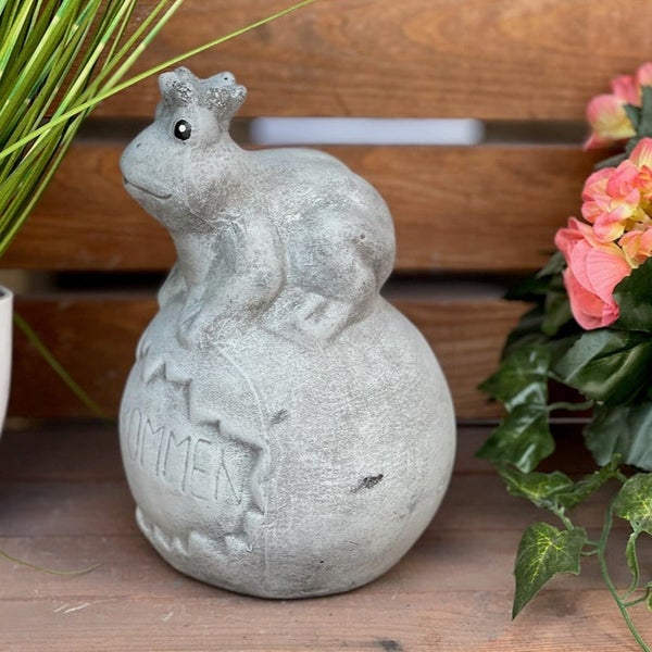 Gartenfigur Frosch aus Kunststein sitzend auf einer Kugel mit Willkommensschriftzug als Dekoration.