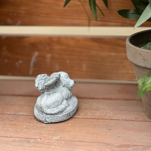 Dekorative Gartenfigur eines liegenden Hundes mit Engelsflügeln aus wetterfestem Steinguss für den Außenbereich.