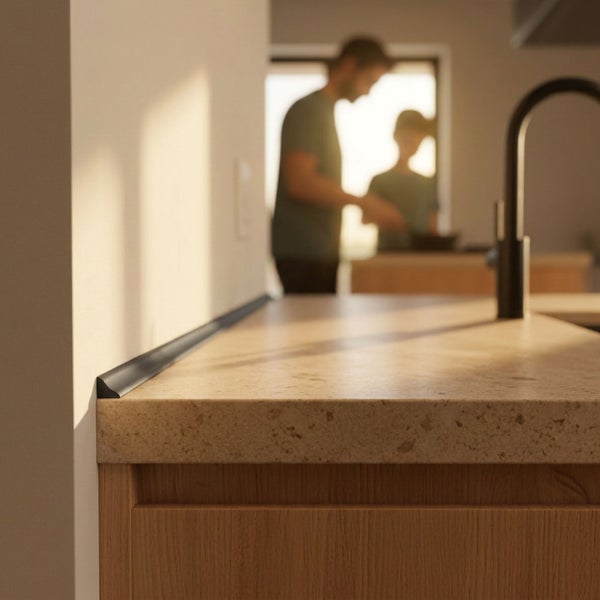 Küchenarbeitsplatte aus Steinoptik mit montiertem dunklem Wandschluss-Profil in einer modernen Küche mit zwei Personen im Hintergrund