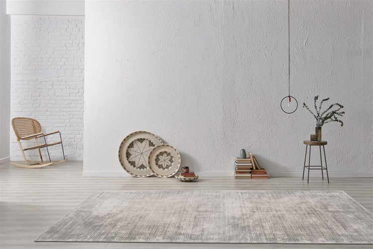 Moderner Wohnraum mit grau und weiß gemustertem Teppich auf hellem Boden, strukturierter Wand, Korbschaukelstuhl und minimalistischer Dekoration.