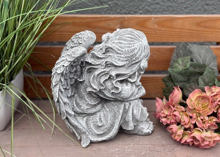 Sitzende Engelsfigur in Steinoptik mit Flügeln, geeignet als Gartendekoration oder Grabschmuck.