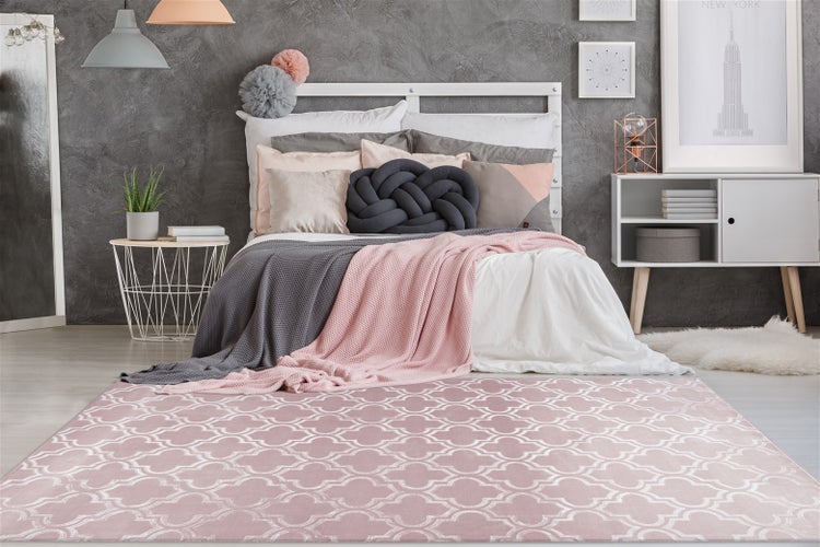 Ein Teppich mit weißem Ziermuster in einem modernen Schlafzimmer mit Bett, Beistelltisch und Sideboard vor einer grauen Wand.