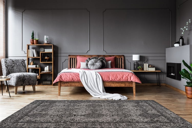 Modernes Schlafzimmer mit dunkelgrauen Wandpaneelen, Holzbett, Kamin, gemustertem Teppich und Holzregal auf hellem Parkettboden.