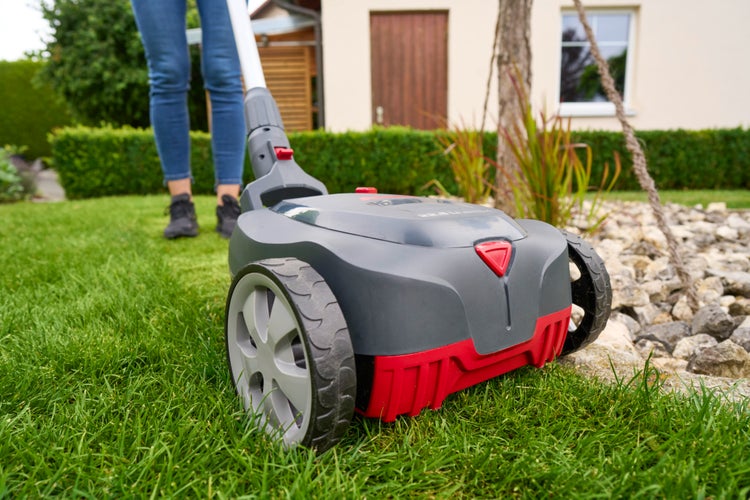 Batteriebetriebener Rasenmäher wird von einer Person auf einer Rasenfläche vor einem Haus in einem Garten verwendet.