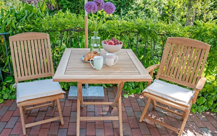 Gartenszene mit Holztisch, zwei Holzstühlen und Dekoration auf einer Terrasse