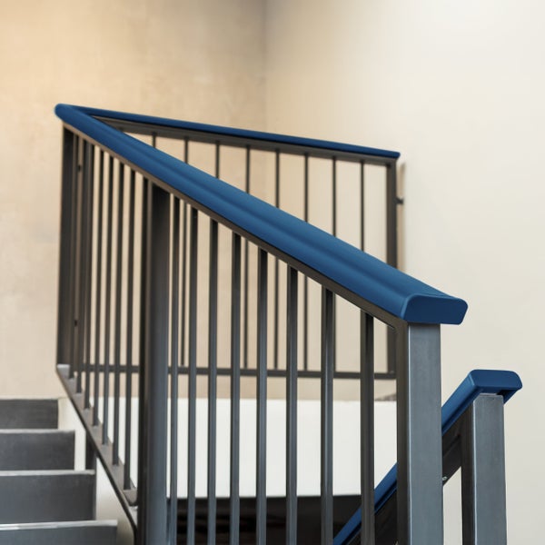 Modernes Treppengeländer aus Metall mit blauem Handlauf und vertikalen Stäben in einem hellen Treppenhaus.