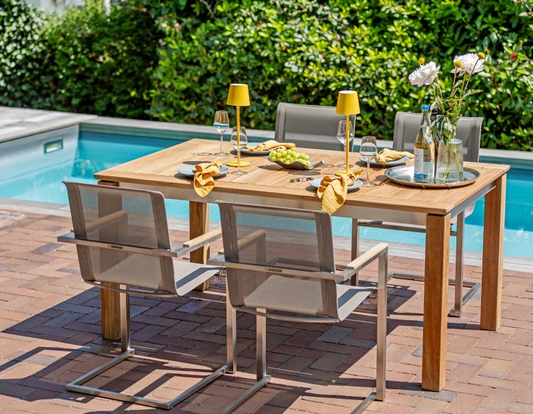 Gartenszene mit Holztisch, Stühlen, Tischlampen und Geschirr neben einem Swimmingpool