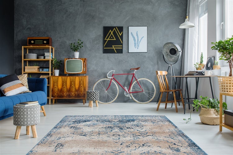 Großer Orientteppich mit Used-Look in Blau und Beige in einem Wohnzimmer mit grauer Strukturwand und Vintage-Möbeln.