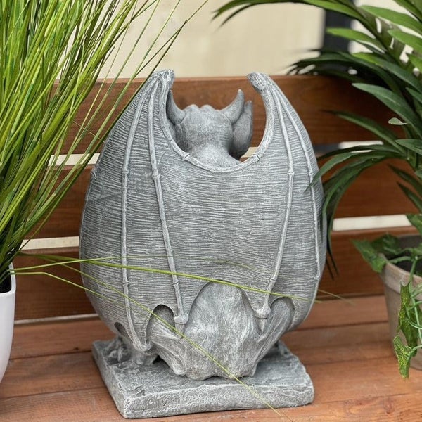 Gartenfigur Wasserspeier aus Stein auf einer Holzterrasse mit Pflanzen im Hintergrund