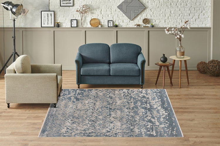 Modernes Wohnzimmer mit blauem Sofa, beigem Sessel und einem rechteckigen Teppich mit abstraktem blau-grauem Muster auf Holzboden.