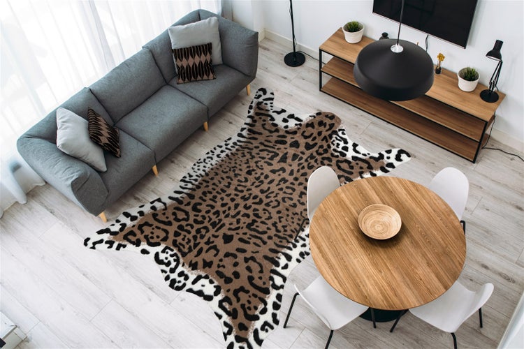 Helles modernes Wohnzimmer mit einem Teppich in Leopardenoptik, einem grauen Textilsofa, einem runden Holzesstisch und einem Sideboard.