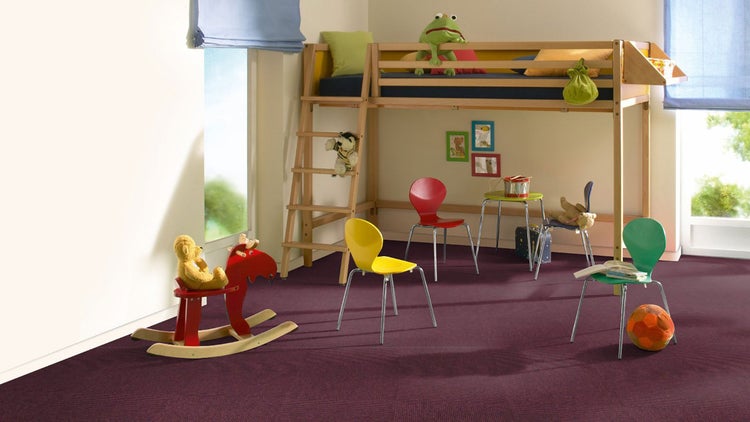 Kinderzimmer mit lila Teppichboden, hölzernem Hochbett, farbigen Stühlen und einem Schaukelpferd.