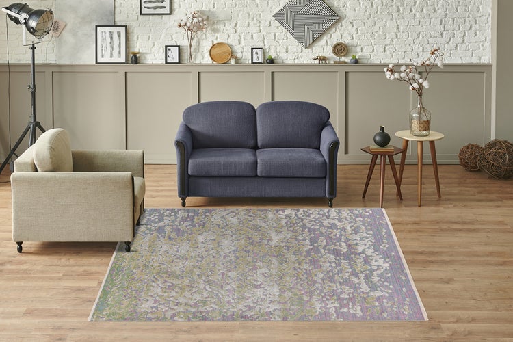 Rechteckiger Teppich mit abstraktem Muster in hellem Wohnzimmer mit blauem Sofa, beigem Sessel, Holzboden und Dekoration.