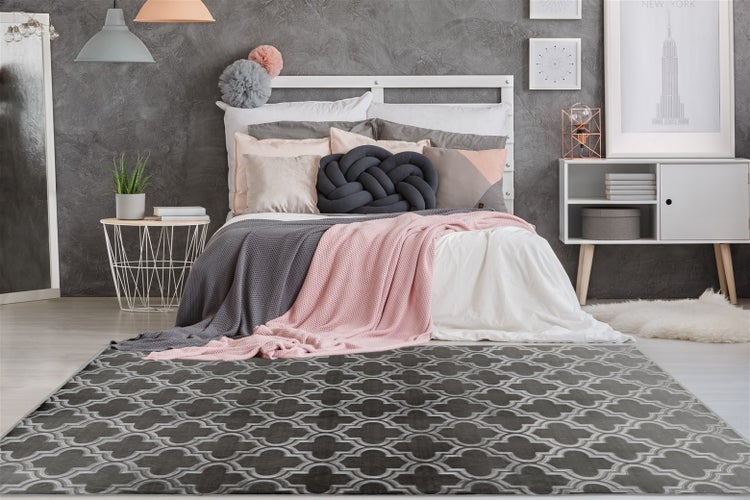 Modernes Schlafzimmer mit grau-weiß gemustertem Teppich, Bett mit Kissen und Decken, weißem Sideboard und strukturierter grauer Wand.