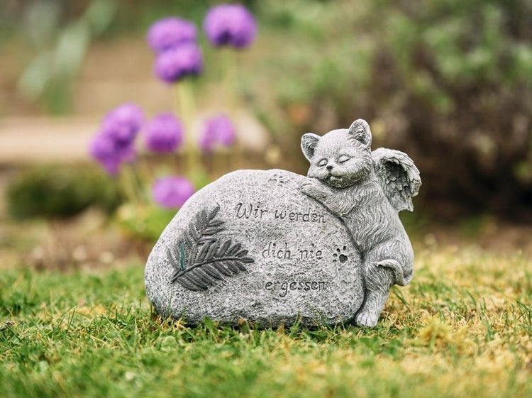 Grabschmuck in Form eines Steins mit schlafender Katzenfigur mit Engelsflügeln und Inschrift Wir werden dich nie vergessen im Garten.