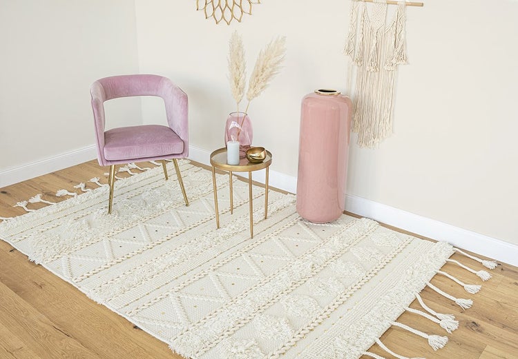 Heller Raum mit strukturiertem Teppich, rosa Samtsessel, goldenem Beistelltisch und großer Bodenvase auf Holzfußboden.