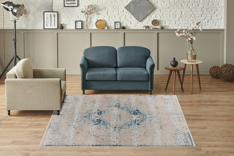 Wohnzimmer mit blau-beigem Vintage-Teppich auf Holzparkett, blauem Sofa und beigem Sessel vor einer weißen Ziegelwand.