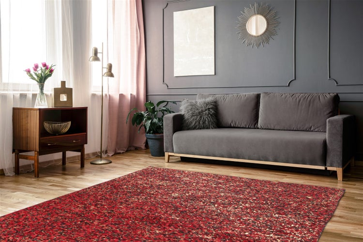 Moderner Wohnraum mit rot gemustertem Teppich auf hellem Holzboden, grauem Sofa, Wand mit Zierleisten und Zimmerpflanze.