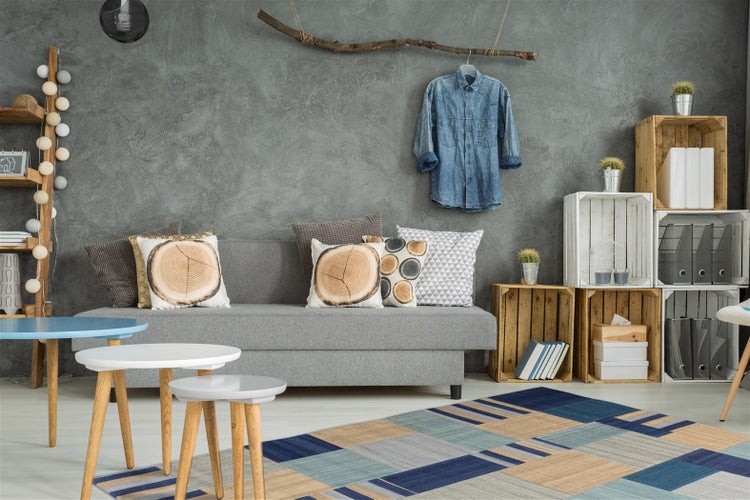 Modernes Wohnzimmer mit grauem Sofa, strukturierten Wänden, Regalen aus Holzkisten, Beistelltischen und einem geometrisch gemusterten Teppich.