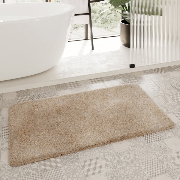 Beige Badematte auf gemusterten Bodenfliesen vor einer weißen Badewanne in einem hellen, modernen Badezimmer.
