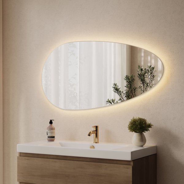 Organisch geformter Wandspiegel mit indirekter LED Beleuchtung über einem Waschplatz im Badezimmer mit Holzwaschtisch und goldener Armatur.