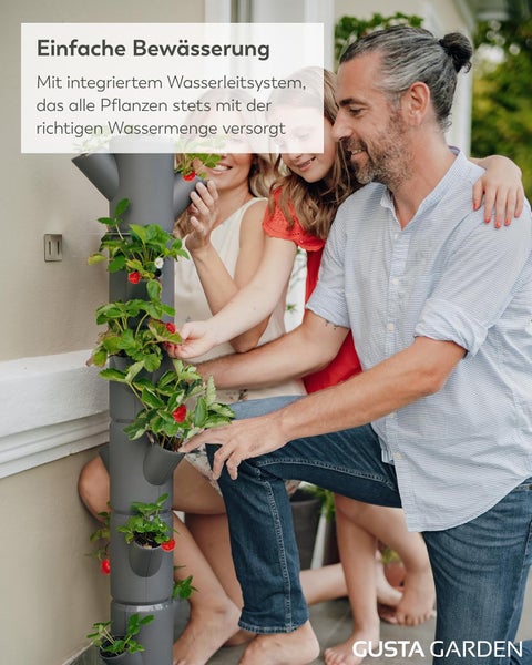 Familie erntet Erdbeeren aus einem grauen vertikalen Pflanzturm mit integriertem Bewässerungssystem auf einer Terrasse. Gusta Garden Logo.
