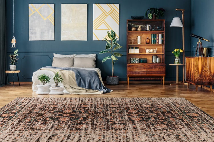 Vintage-Teppich mit verwaschenem Muster auf Holzboden in einem Zimmer mit dunkelblauer Wand, Holzmöbeln und verschiedenen Zimmerpflanzen.