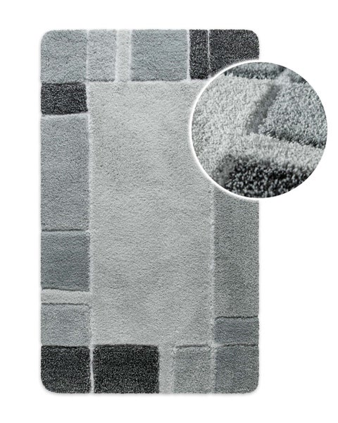 Rechteckige Hochflor-Badematte mit geometrischem Karomuster in Grautönen und einer Detailansicht der weichen Struktur.