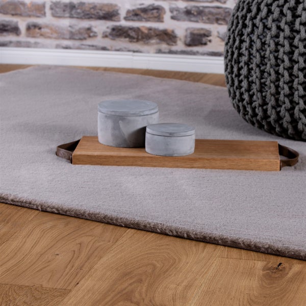 Weicher Teppich auf einem Holzfußboden mit einem Holztablett, zwei Betonbehältern und einem Strickpouf vor einer Ziegelwand.