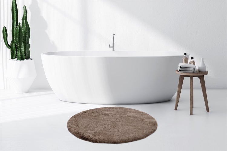 Runder, brauner Badteppich in einem hellen Badezimmer mit freistehender Badewanne und Kaktus.