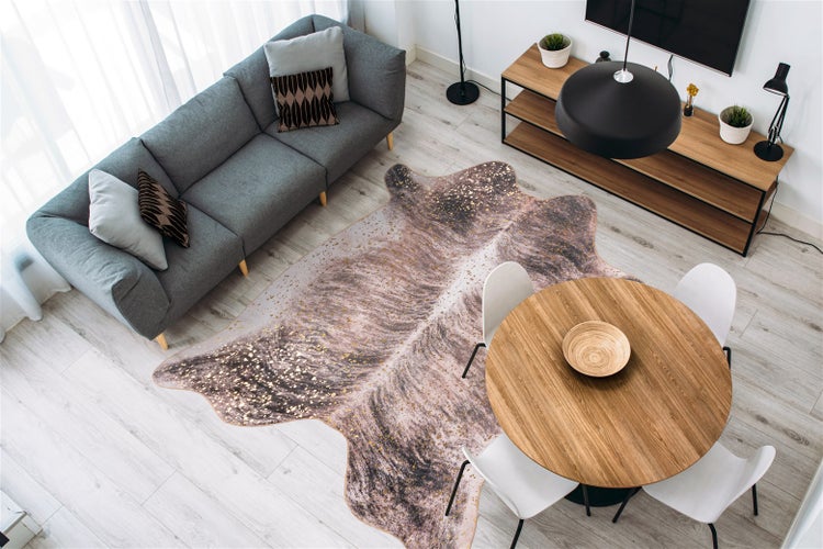 Modernes Wohnzimmer mit grauem Sofa, rundem Holztisch mit weißen Stühlen und einem Teppich in Tierhautform auf hellem Boden.