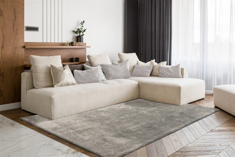 Modernes helles Wohnzimmer mit Ecksofa, Zierkissen und Teppich auf Parkettboden. Wandregal aus Holz mit Pflanze und Vorhängen.