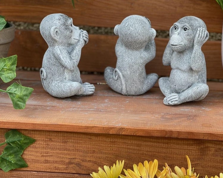 Set aus drei Affenfiguren aus Kunststein in der Darstellung der drei weisen Affen als Gartendekoration auf einer Holzoberfläche.