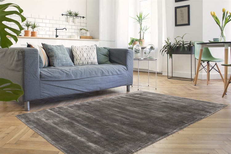 Moderner Wohnbereich mit grauem Teppich auf Fischgrätparkett, grauem Sofa mit Kissen und Zimmerpflanzen in hellem, organisiertem Ambiente.