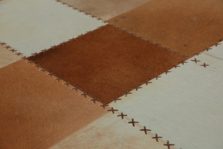 Detailaufnahme eines Patchwork-Teppichs aus Kuhfell mit dekorativen Kreuzstichen.