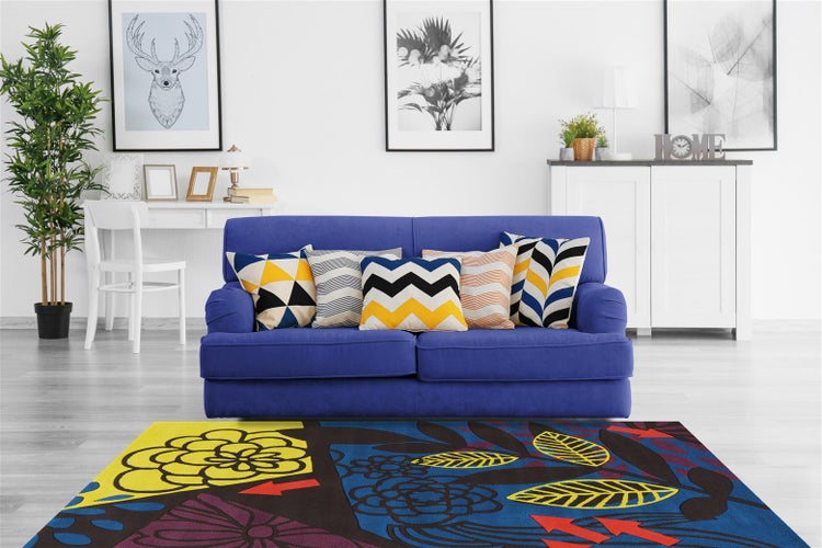 Modernes Wohnzimmer mit blauem Sofa, gemusterten Zierkissen und einem großen bunten Teppich mit floralen und geometrischen Mustern.