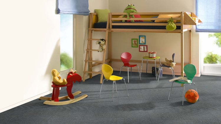 Kinderzimmer mit dunkelgrauen Teppichfliesen, einem Hochbett aus Holz und bunten Stühlen.