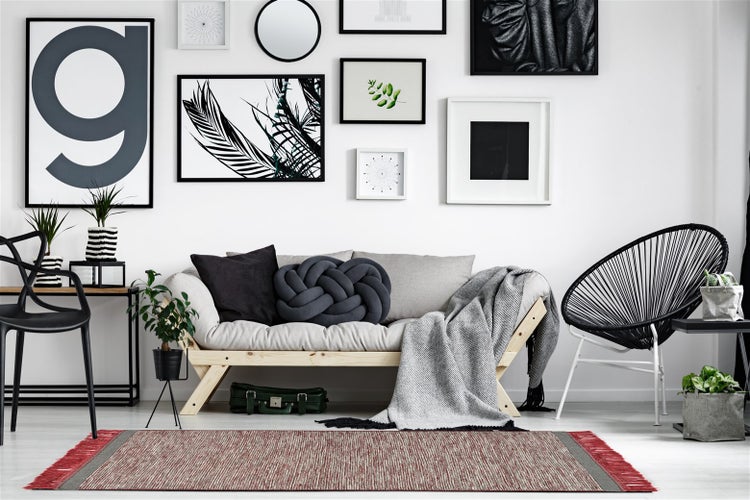 Moderner Wohnbereich mit hellem Sofa, Bilderwand und einem rechteckigen Teppich in Rot und Grau mit Fransen.