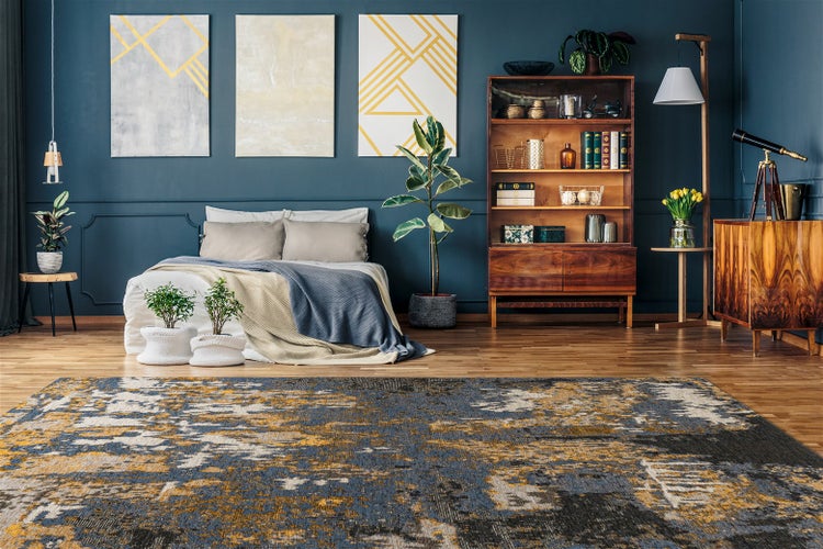 Moderner Wohnbereich mit abstrakt gemustertem Teppich auf Holzboden vor einer dunklen Wand mit Kunstwerken und einem Bett.