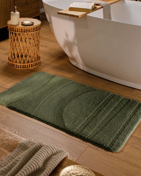 Rechteckige grüne Badematte mit geometrischem Muster auf einem Holzfußboden neben einer freistehenden weißen Badewanne.