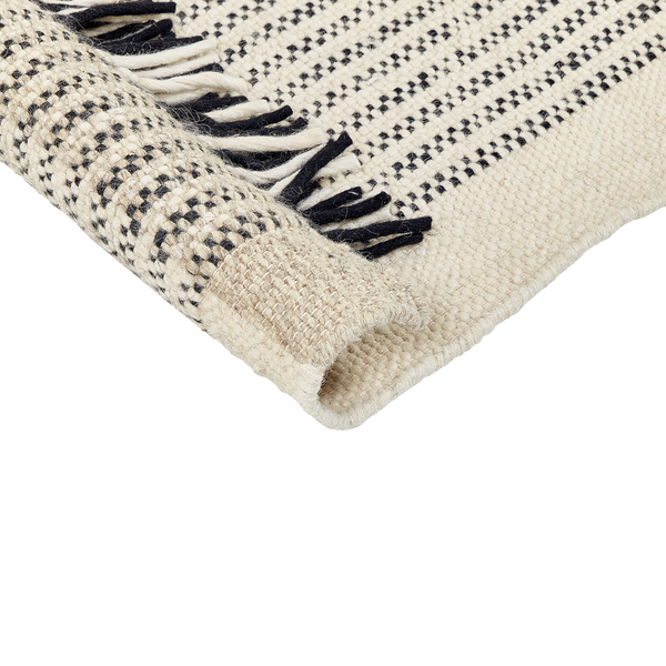 Gewebter Teppich mit Punktmuster und Fransen, Detailaufnahme mit umgeschlagener Ecke.