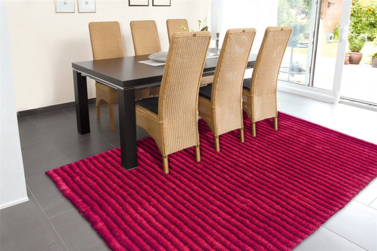 Gestreifter Teppich in Rot in einem Esszimmer mit dunklem Holztisch, Rattanstühlen und grauem Fliesenboden.