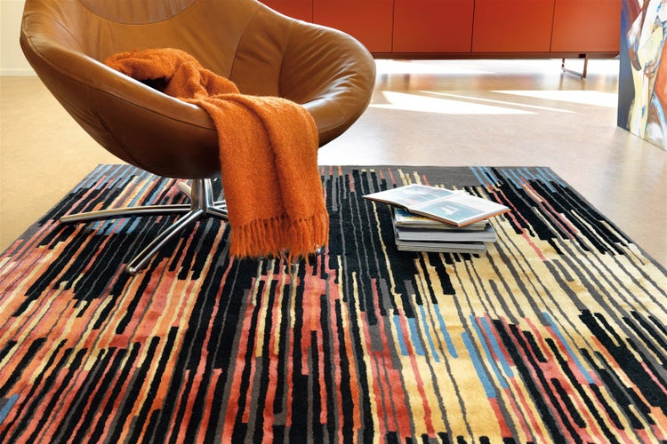 Moderner gemusterter Teppich mit bunten vertikalen Streifen in einer Wohnzimmerszene mit einem Sessel.