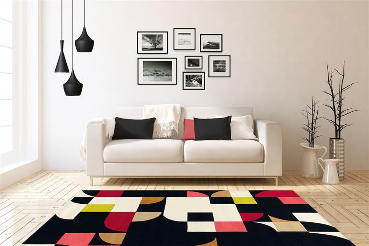 Modernes Wohnzimmer mit weißem Sofa, buntem geometrischem Teppich, Bildergalerie und schwarzen Pendelleuchten auf hellem Holzboden.